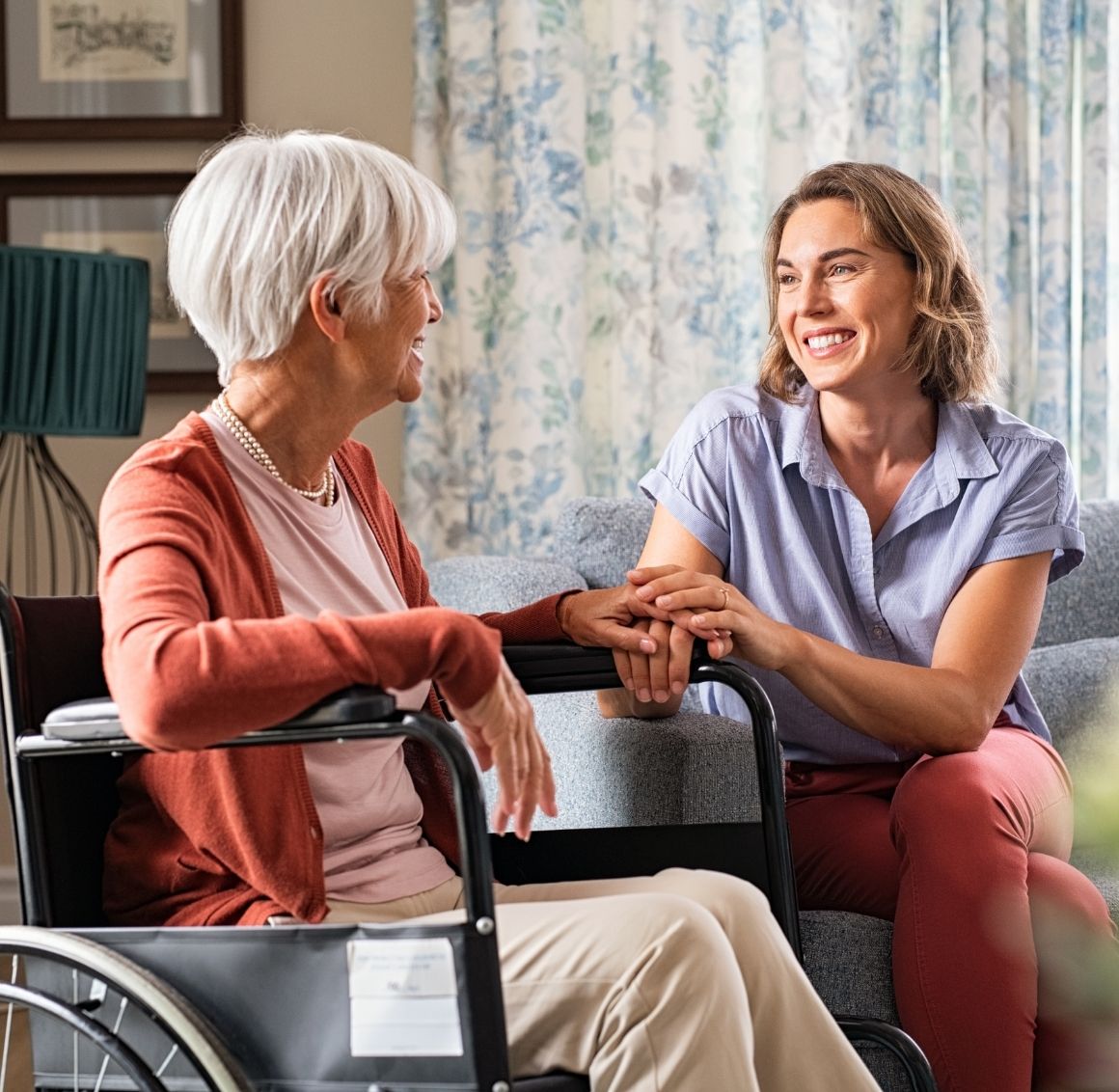 compassionate in-home caregiver visit Caregiver with a satisfying job warmly talking with an elderly woman on a couch during an in-home care visit.