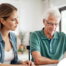 Adult daughter and senior father talking at a kitchen table while comparing home care vs assisted living